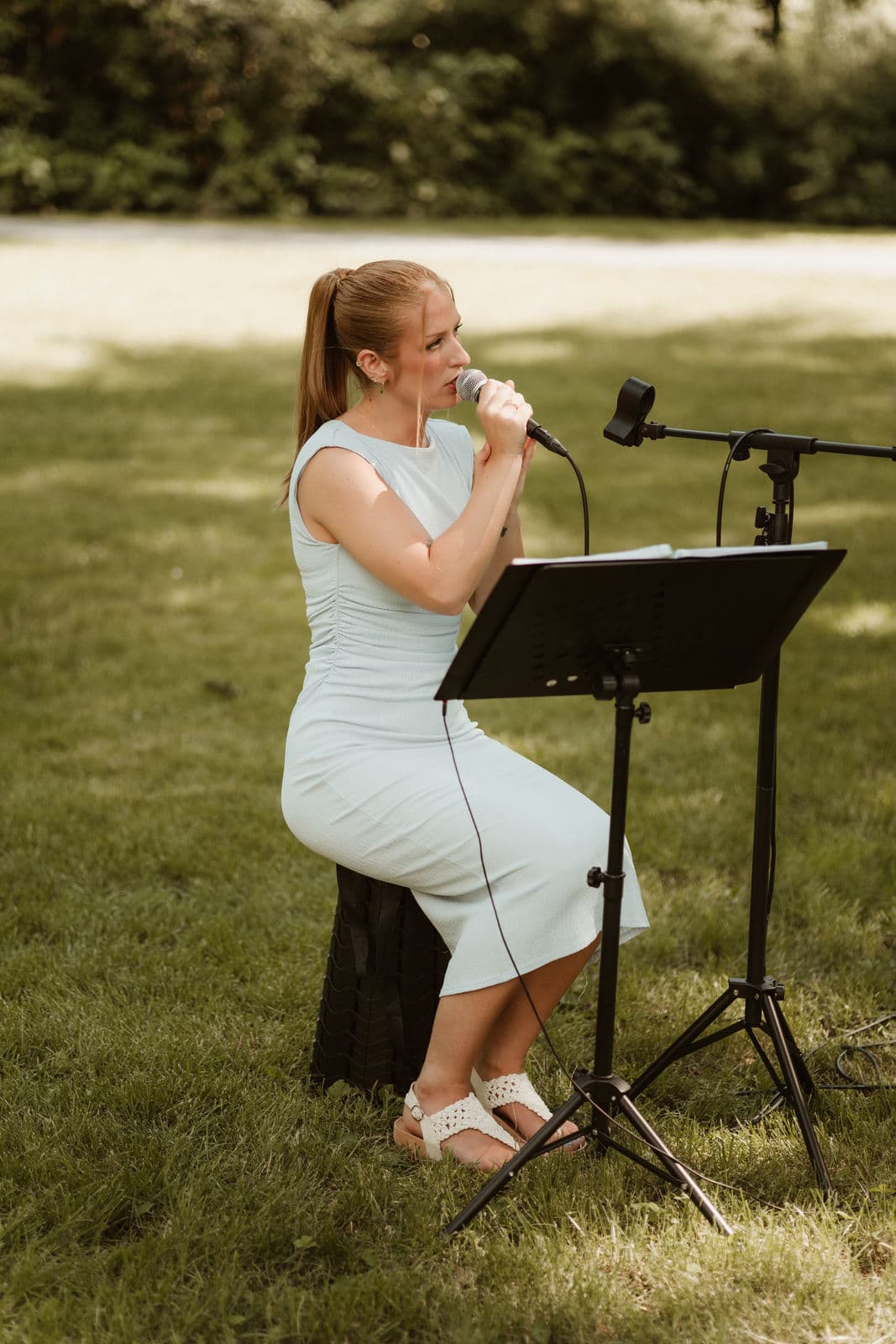 Jasmin Nell singt live ins Mikrofon, im Hintergrund die Wiese vor der Trauungslocation